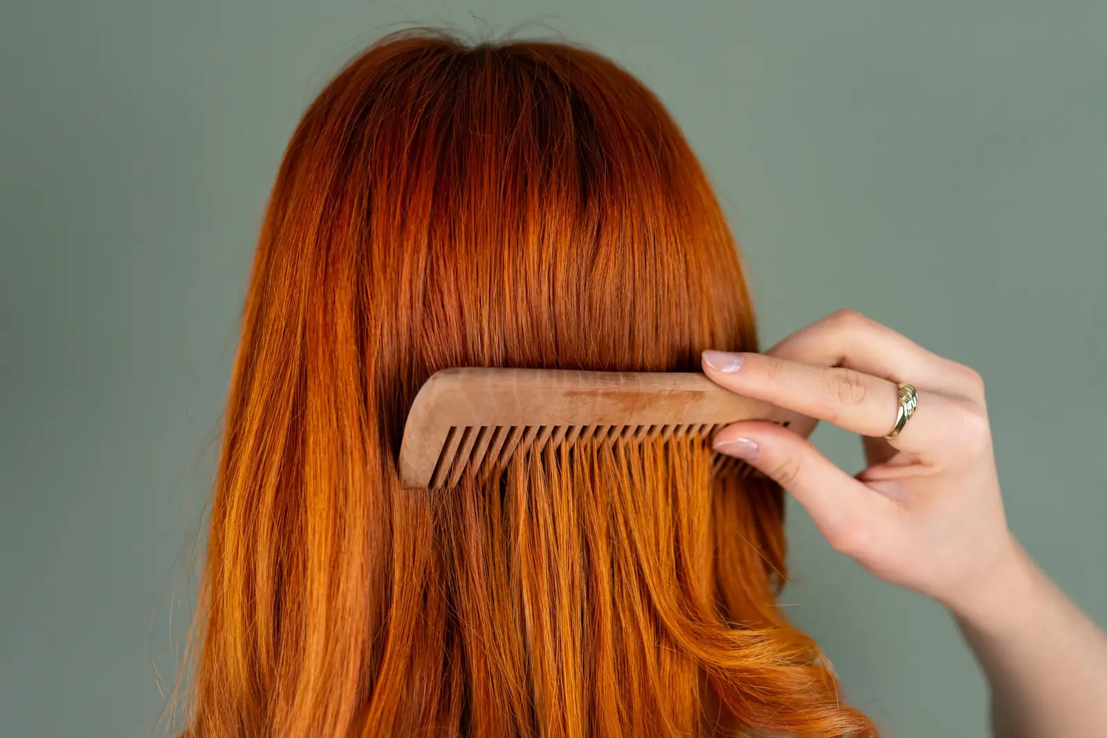 Mulher de cabelo ruivo, vista de costas, penteia os fios com um pente de madeira