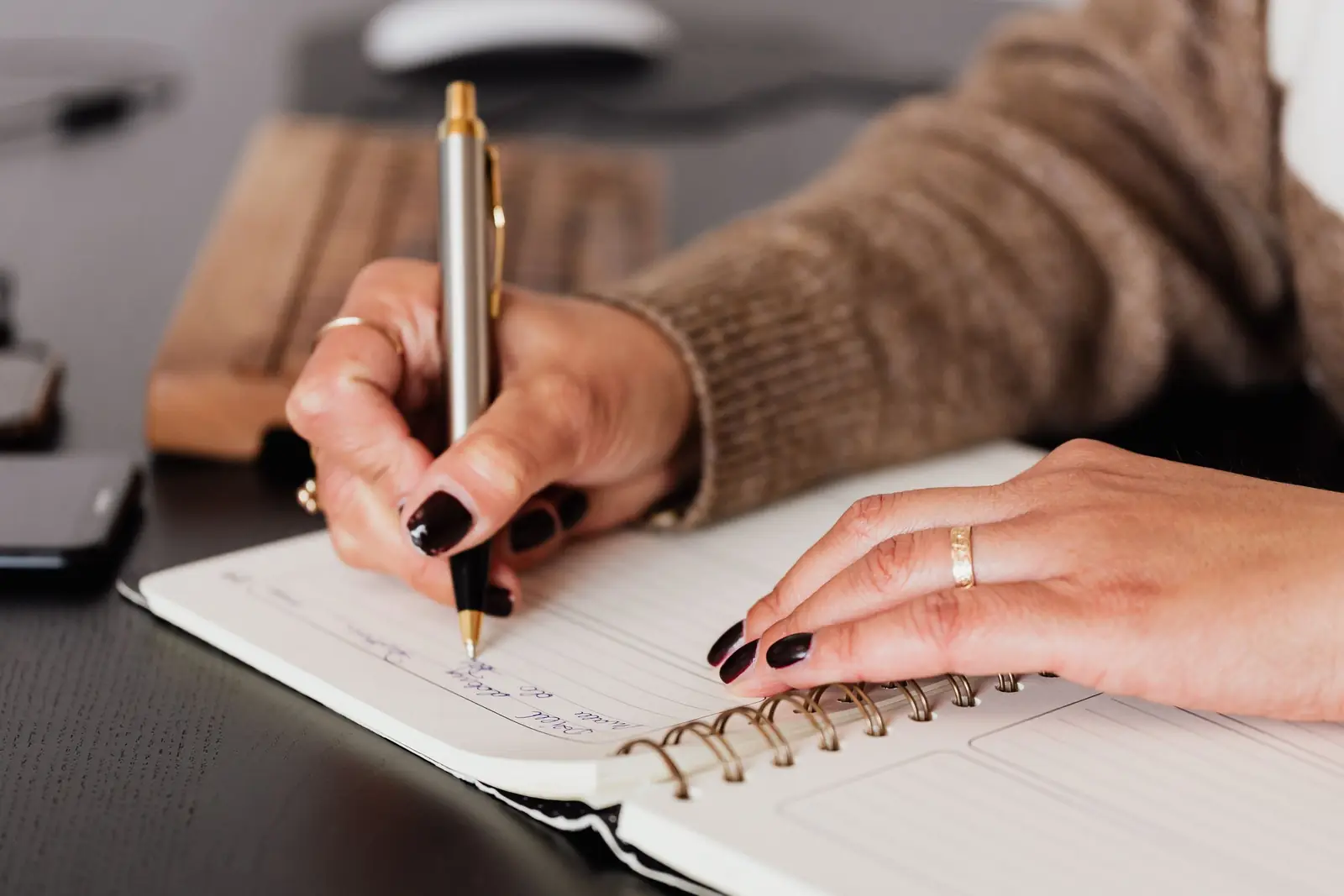 Mãos de mulher fazendo anotações em um caderno de espiral sobre a mesa