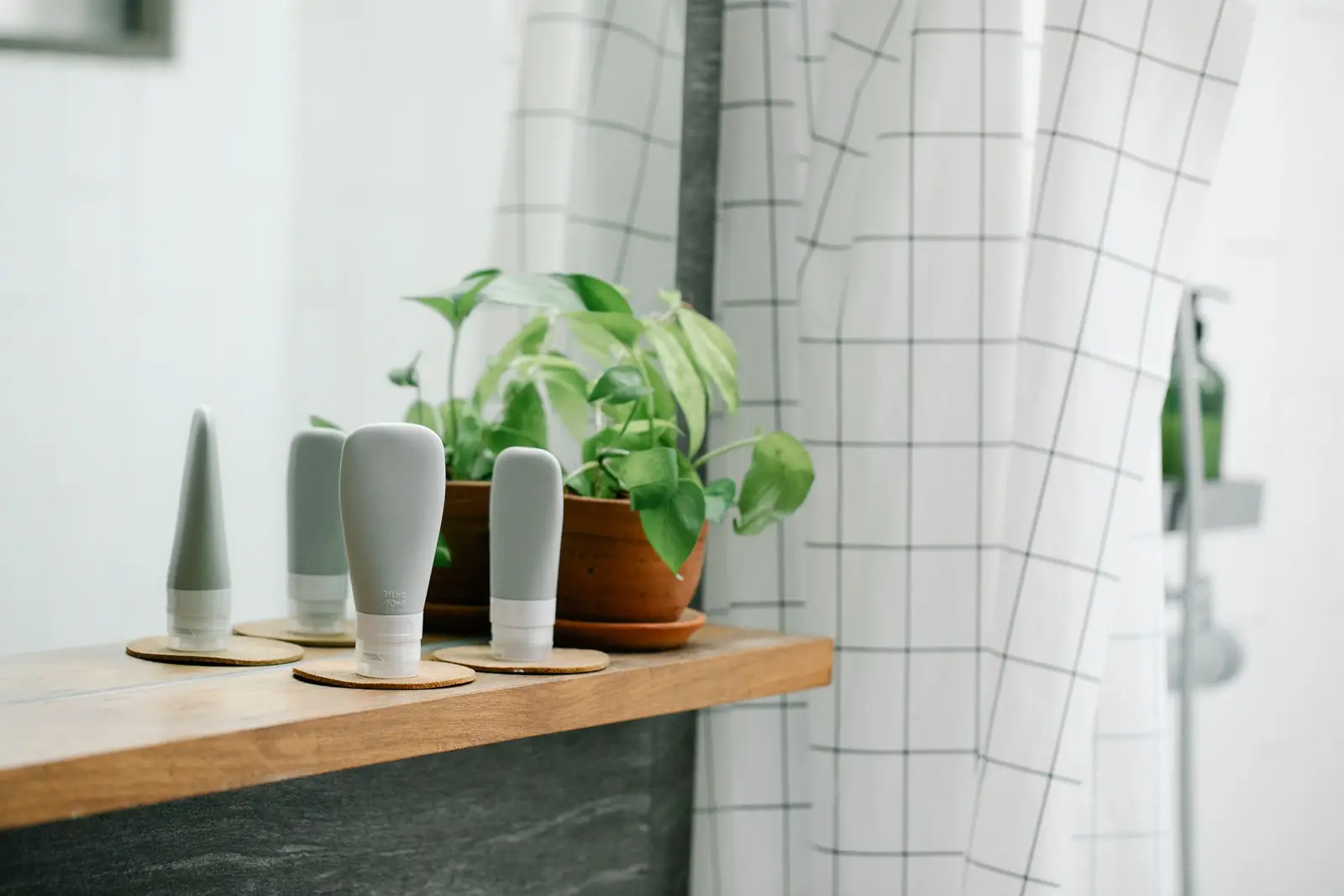 Prateleira de banheiro com frascos sem rótulo e um vaso de planta ao lado da cortina