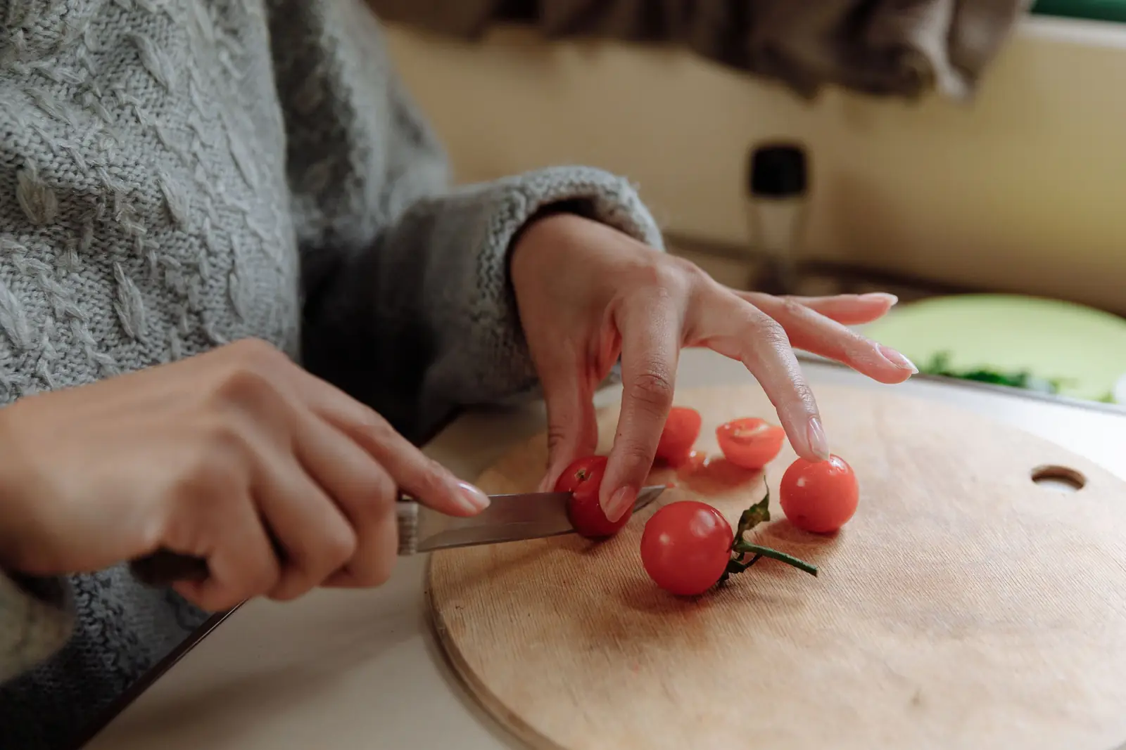 Mãos de mulher cortando tomates-cereja em uma tábua de madeira na cozinha